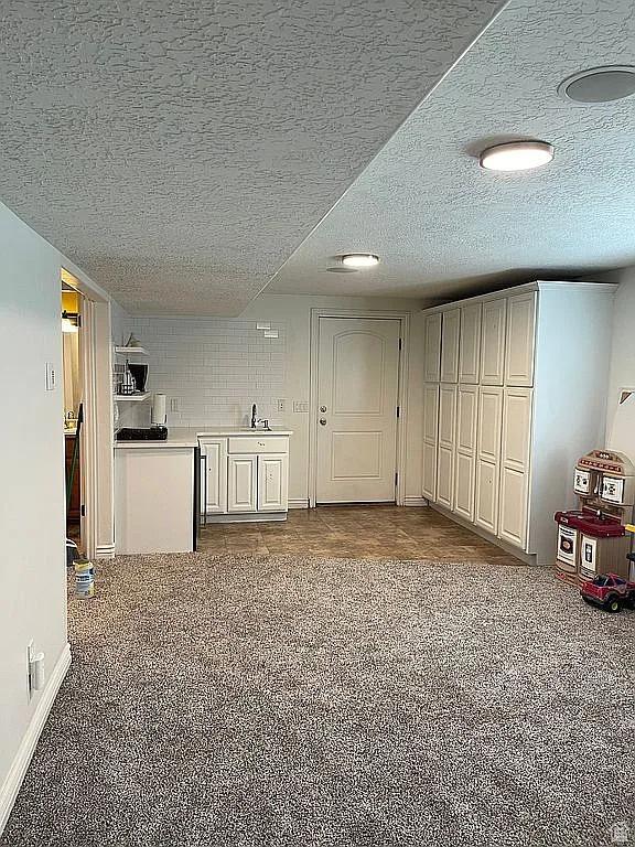 unfurnished living room with sink, carpet floors, and a textured ceiling