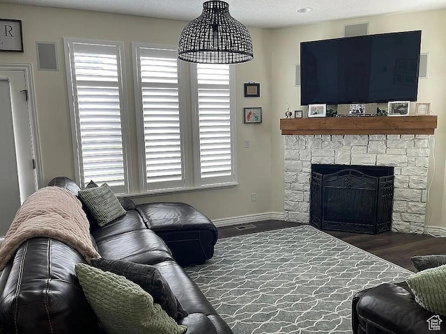 living room featuring plenty of natural light, dark hardwood / wood-style flooring, and a stone fireplace