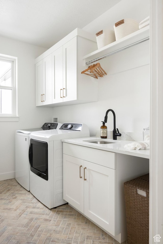 clothes washing area featuring a sink, baseboards, separate washer and dryer, cabinet space, and brick floor