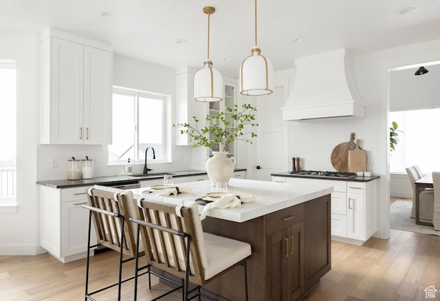 kitchen featuring a breakfast bar, a sink, premium range hood, light wood-style flooring, and white cabinetry