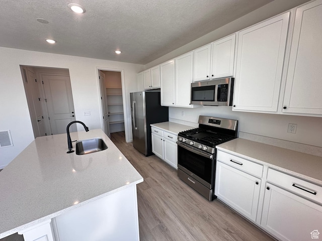 kitchen featuring appliances with stainless steel finishes, a sink, light wood-style floors, white cabinetry, and recessed lighting