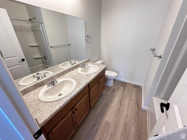 bathroom featuring wood finished floors, double vanity, toilet, baseboards, and shower / bath combination
