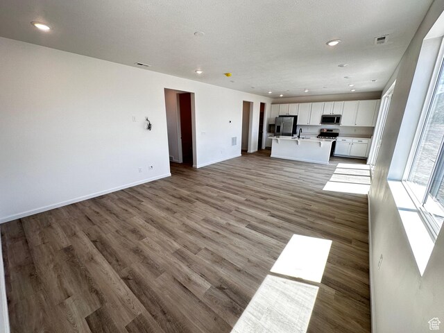 unfurnished living room featuring a sink, recessed lighting, light wood-type flooring, and baseboards