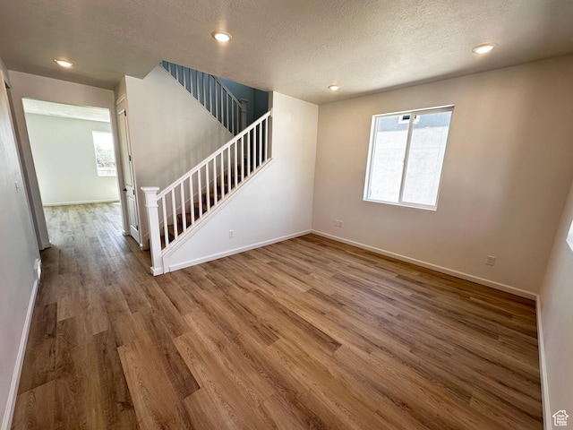 unfurnished living room with wood finished floors, baseboards, stairway, a textured ceiling, and recessed lighting