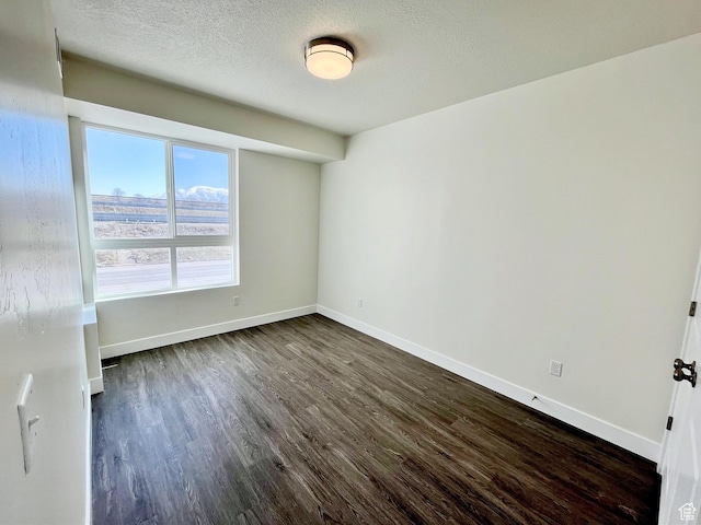 unfurnished room with a textured ceiling, dark wood-style floors, and baseboards