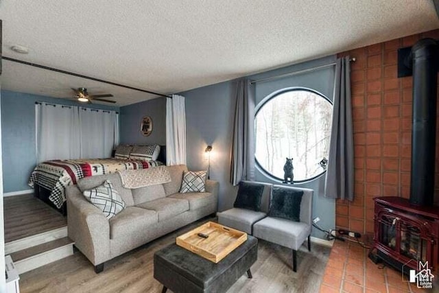 living room with hardwood / wood-style floors, ceiling fan, a textured ceiling, and a wood stove