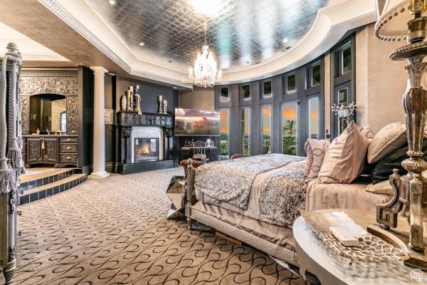 carpeted bedroom featuring a raised ceiling, ornamental molding, a chandelier, and ornate columns