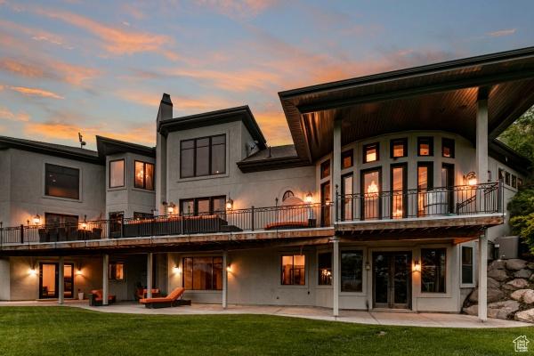 back house at dusk with a lawn, a balcony, and a patio area