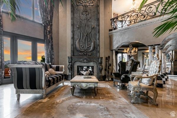 sitting room featuring a towering ceiling, a premium fireplace, a chandelier, and decorative columns