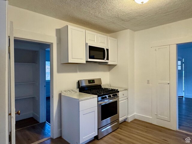 2721 Gramercy Ave, Ogden, UT 84403 - kitchen featuring white microwave, stainless steel range with gas stovetop, dark wood-type flooring, white cabinets, and light countertops
