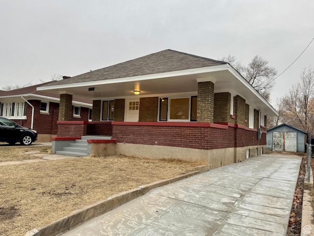 view of front of property with a porch, driveway, brick siding, and an outdoor structure