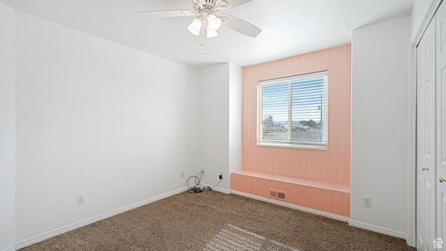 carpeted spare room featuring ceiling fan and wood walls