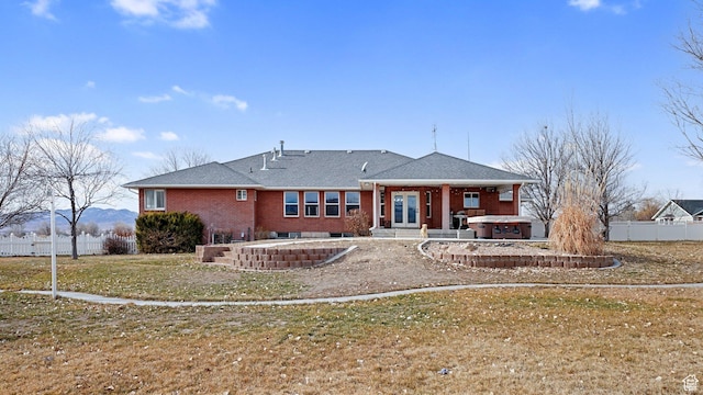 rear view of house with a hot tub and a yard