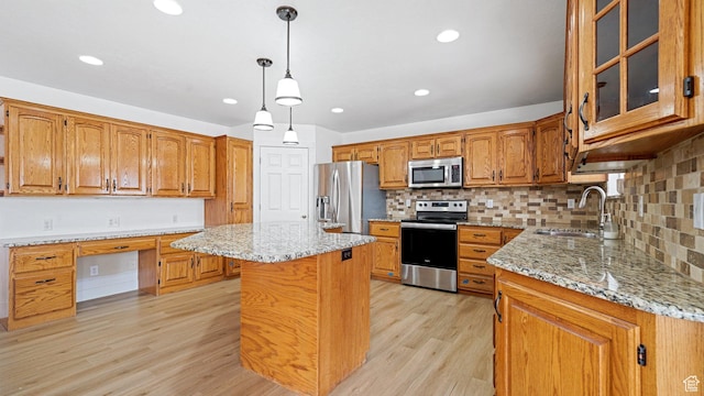 kitchen featuring sink, stainless steel appliances, built in desk, light stone countertops, and a kitchen island