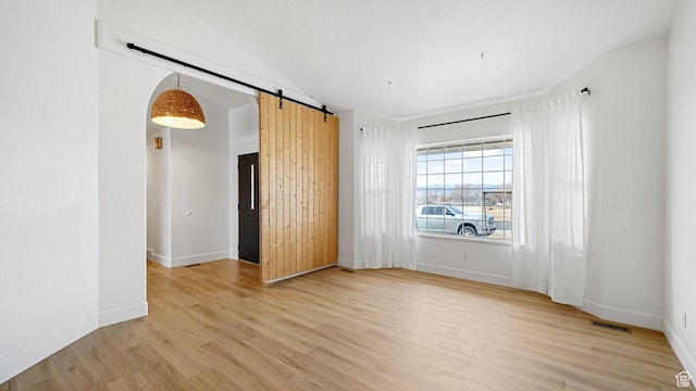 spare room featuring a barn door, vaulted ceiling, and light hardwood / wood-style flooring