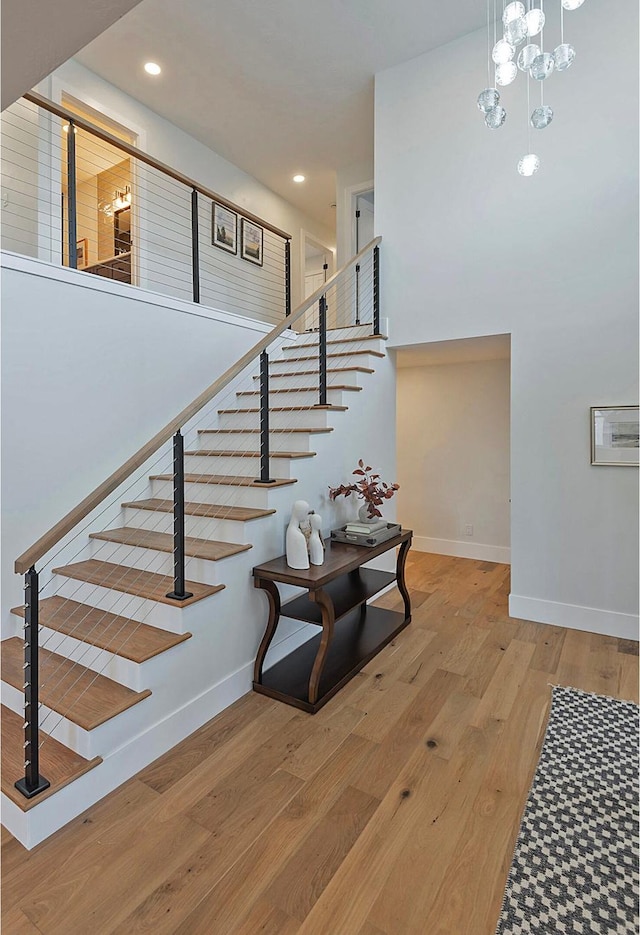 staircase featuring baseboards, recessed lighting, a towering ceiling, and wood finished floors