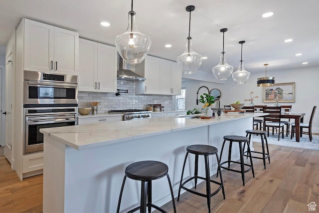 kitchen with light stone counters, light wood-style floors, white cabinetry, recessed lighting, and a center island with sink