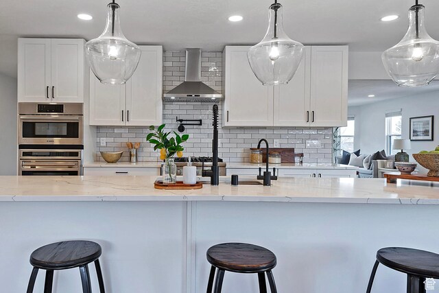 kitchen with recessed lighting, white cabinetry, and wall chimney range hood