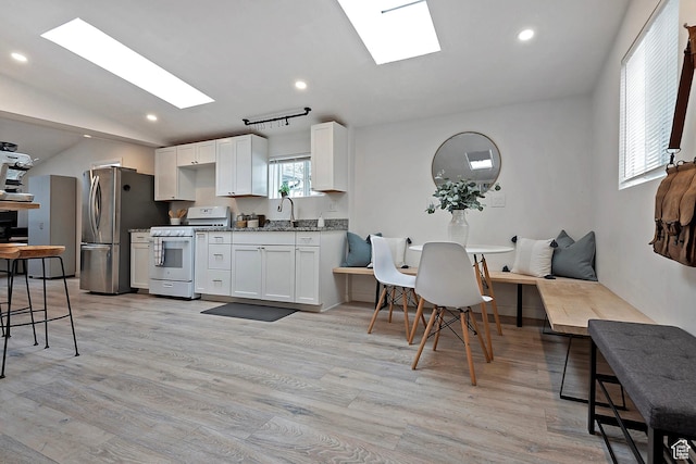 kitchen with freestanding refrigerator, white range with gas stovetop, white cabinets, vaulted ceiling with skylight, and light wood finished floors