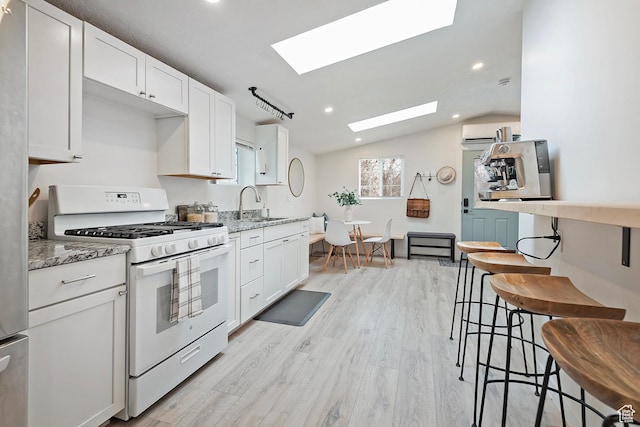 kitchen with a sink, white cabinetry, light stone counters, white gas range oven, and light wood-style flooring