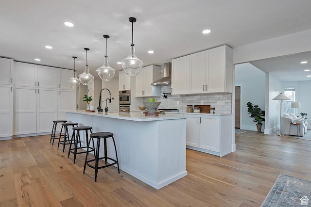kitchen with light countertops, a sink, wall chimney exhaust hood, and light wood-style floors