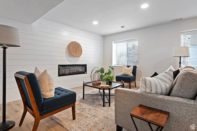 living room featuring recessed lighting, visible vents, a glass covered fireplace, and light wood finished floors