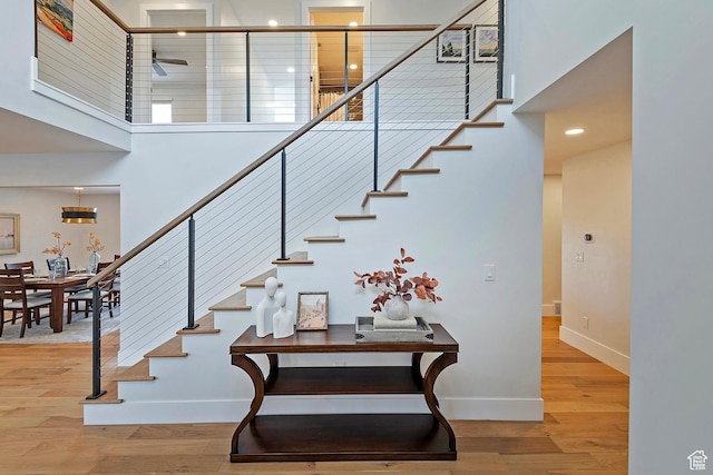 stairway with a ceiling fan, baseboards, wood finished floors, and a towering ceiling