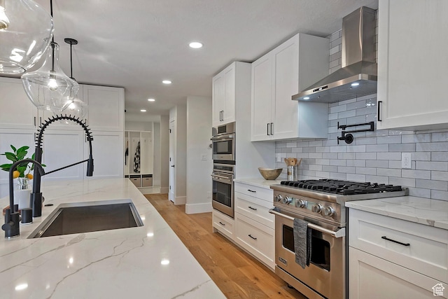 kitchen featuring appliances with stainless steel finishes, tasteful backsplash, a sink, light wood-style floors, and wall chimney exhaust hood