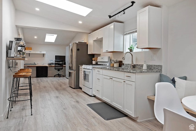 kitchen featuring vaulted ceiling with skylight, white gas stove, a sink, freestanding refrigerator, and white cabinetry