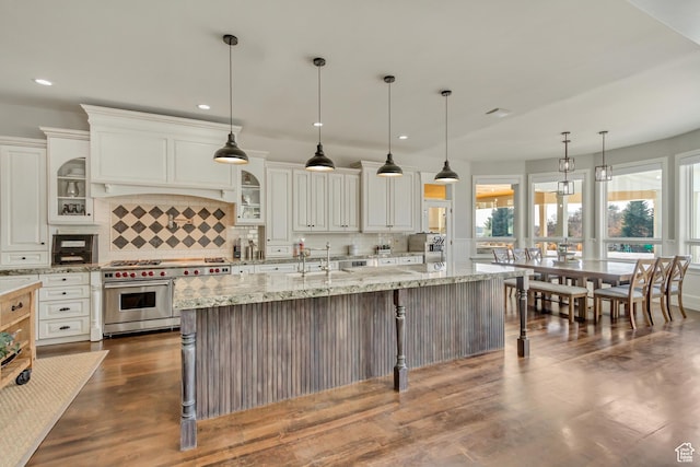 kitchen featuring a breakfast bar area, white cabinetry, light stone countertops, decorative light fixtures, and range with two ovens