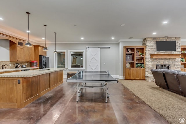 playroom with crown molding, a barn door, sink, and a stone fireplace