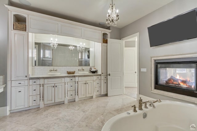 bathroom with a multi sided fireplace, tasteful backsplash, a chandelier, a tub to relax in, and vanity