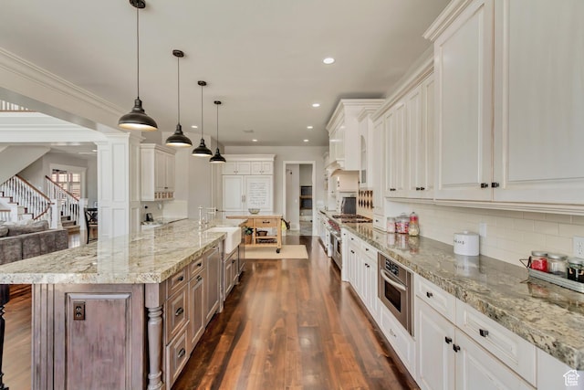 kitchen featuring a spacious island, stainless steel oven, hanging light fixtures, light stone countertops, and white cabinets