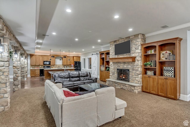 carpeted living room featuring a fireplace, ornamental molding, and a barn door