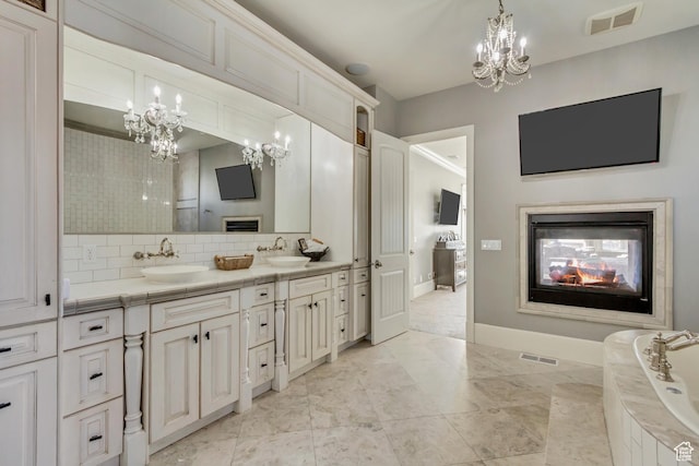 bathroom with an inviting chandelier, a multi sided fireplace, vanity, and backsplash