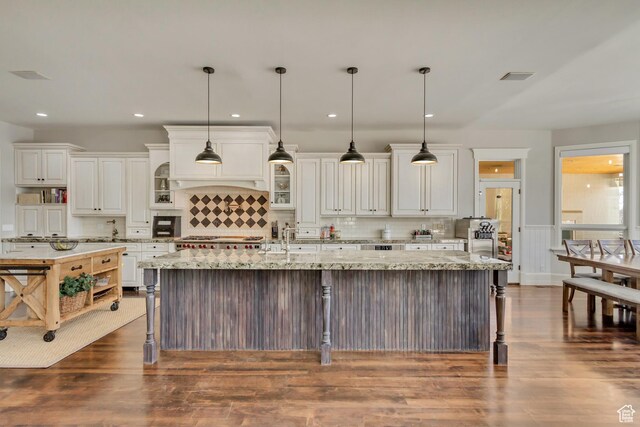 kitchen with a large island, white cabinets, light stone counters, and decorative light fixtures