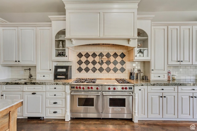 kitchen with sink, range with two ovens, light stone counters, decorative backsplash, and white cabinets