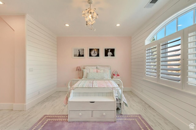 bedroom with wooden walls, a notable chandelier, and light wood-type flooring