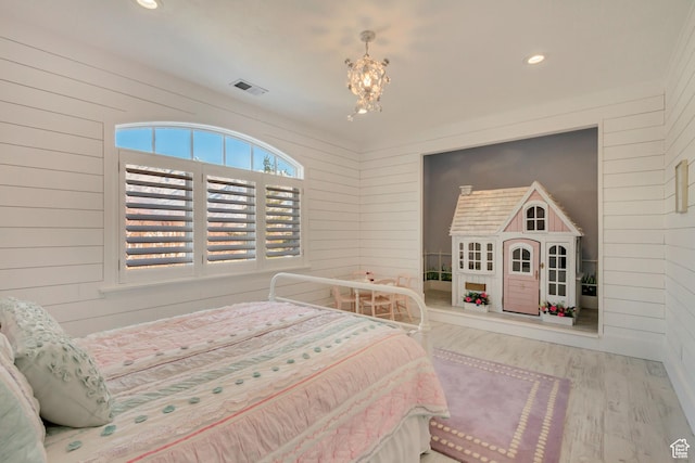 bedroom with a chandelier, light wood-type flooring, and wood walls