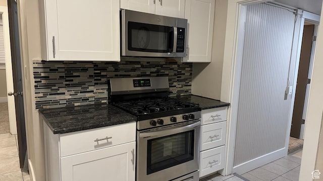 kitchen featuring dark stone countertops, stainless steel appliances, white cabinets, and light tile patterned flooring