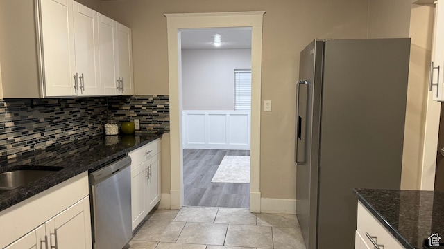 kitchen featuring tasteful backsplash, light tile patterned floors, dark stone counters, stainless steel appliances, and white cabinets