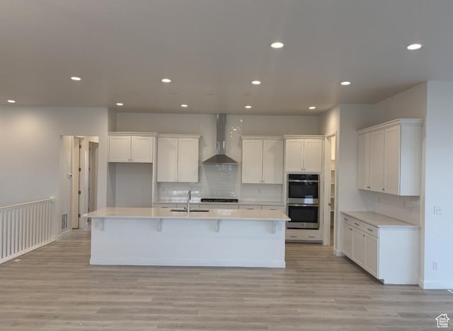 284 E Polaris Dr Unit 112, Saratoga Springs, UT 84045 - kitchen with stainless steel double oven, white cabinetry, an island with sink, and wall chimney exhaust hood