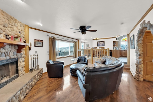living room with crown molding, baseboard heating, hardwood / wood-style flooring, ceiling fan, and a fireplace