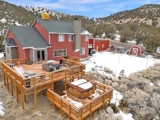 snow covered house with a hot tub, a deck with mountain view, and a shed