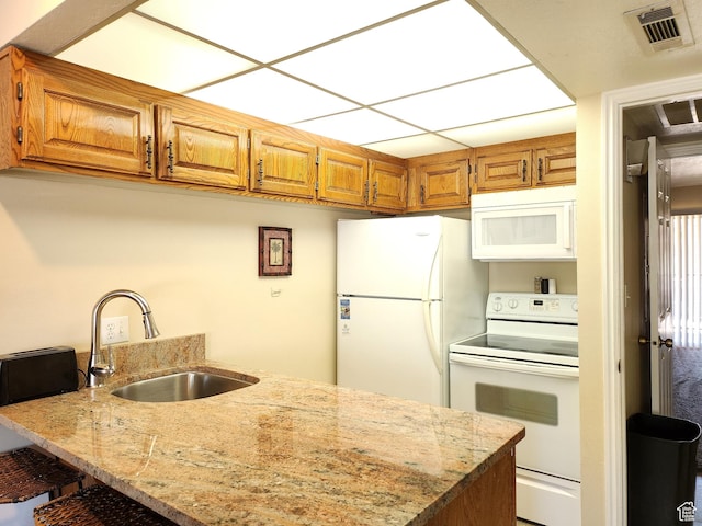 kitchen with light stone counters, sink, white appliances, and kitchen peninsula