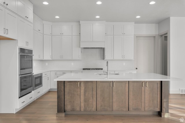 kitchen with a kitchen island with sink, sink, white cabinets, and double oven