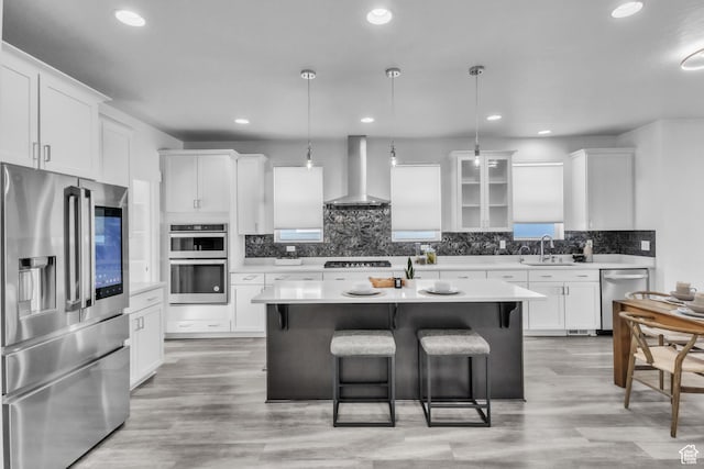 kitchen with decorative light fixtures, appliances with stainless steel finishes, a center island, and wall chimney exhaust hood