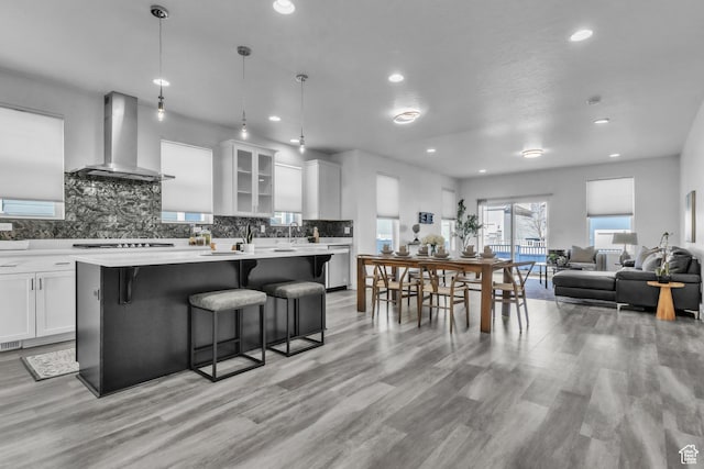 kitchen featuring white cabinetry, decorative light fixtures, wall chimney exhaust hood, and a kitchen bar