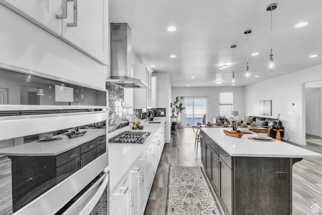 kitchen featuring pendant lighting, white cabinets, a center island, and wall chimney exhaust hood