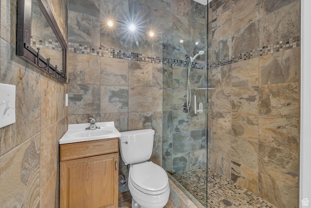bathroom with tile walls, toilet, tiled shower, and vanity